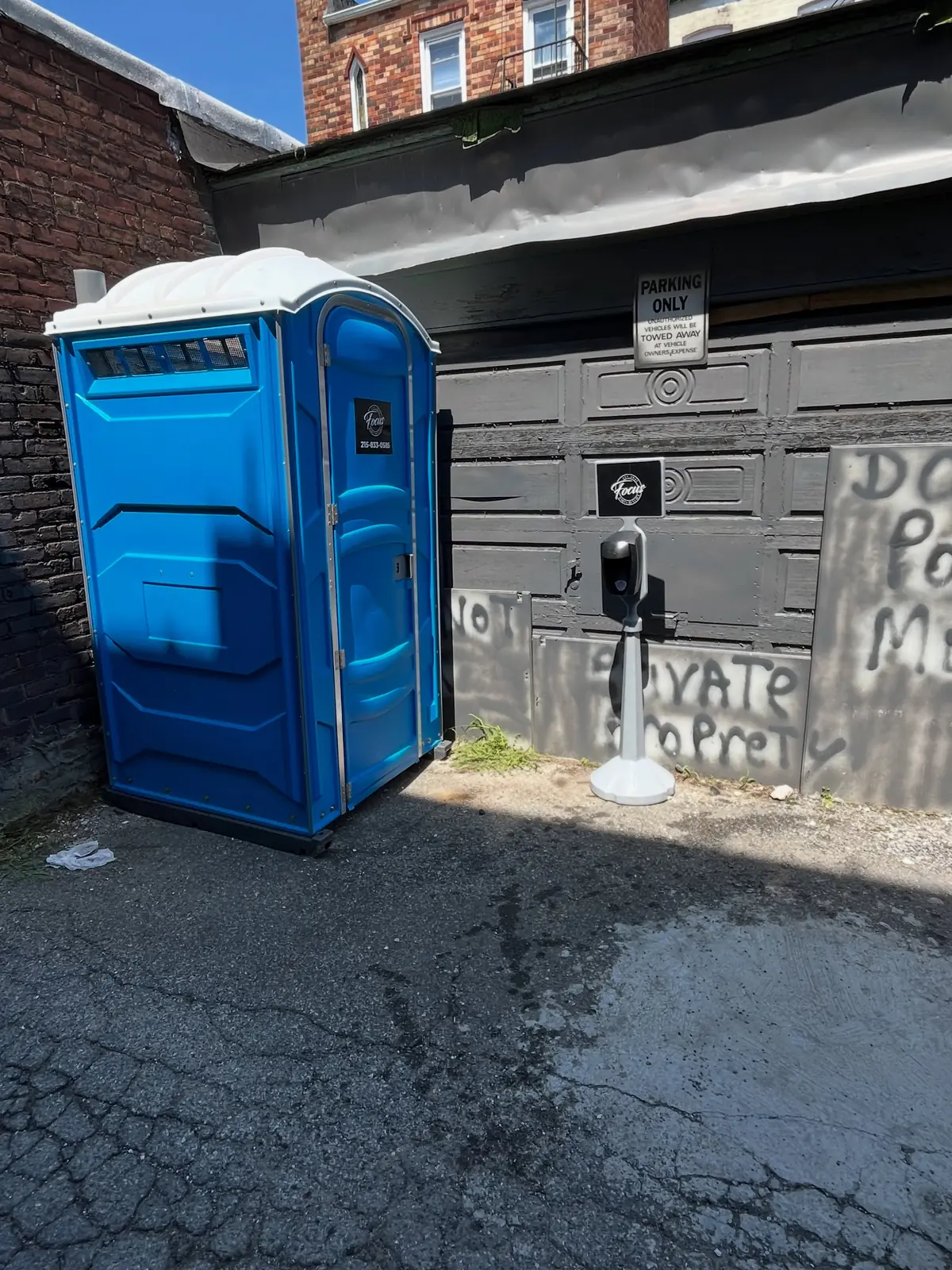 Blue porta potty placed on asphalt beside a brick building