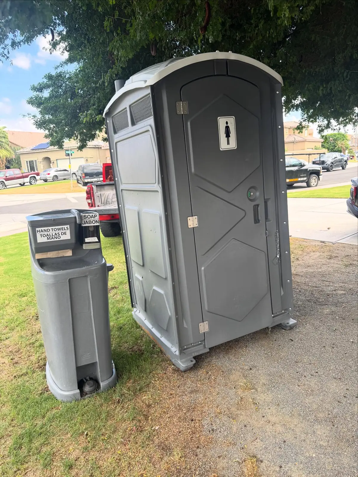Gray porta potty with a foot-pump handwashing station beside it