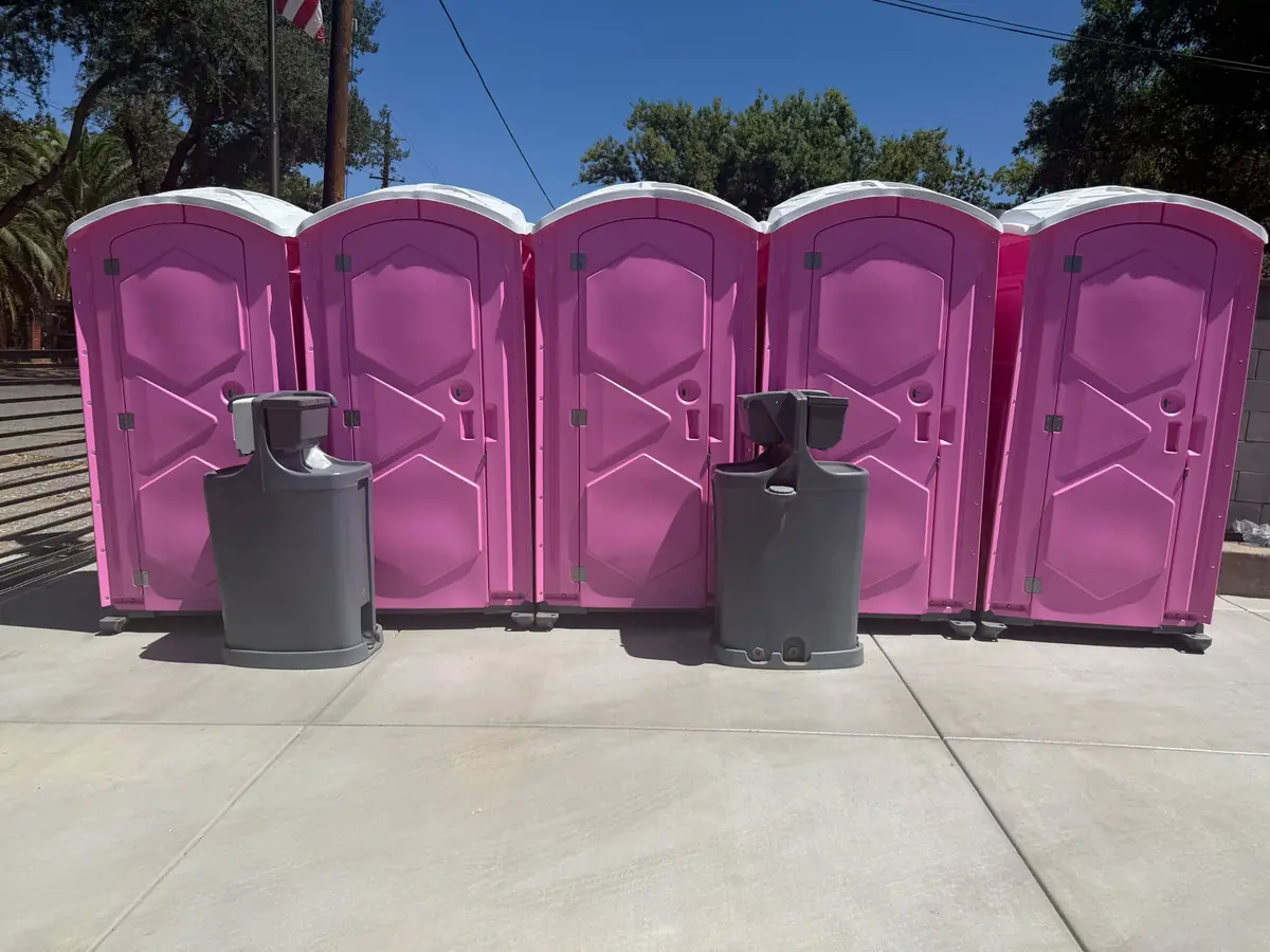 Row of pink porta potties with two handwashing stations on a concrete pad